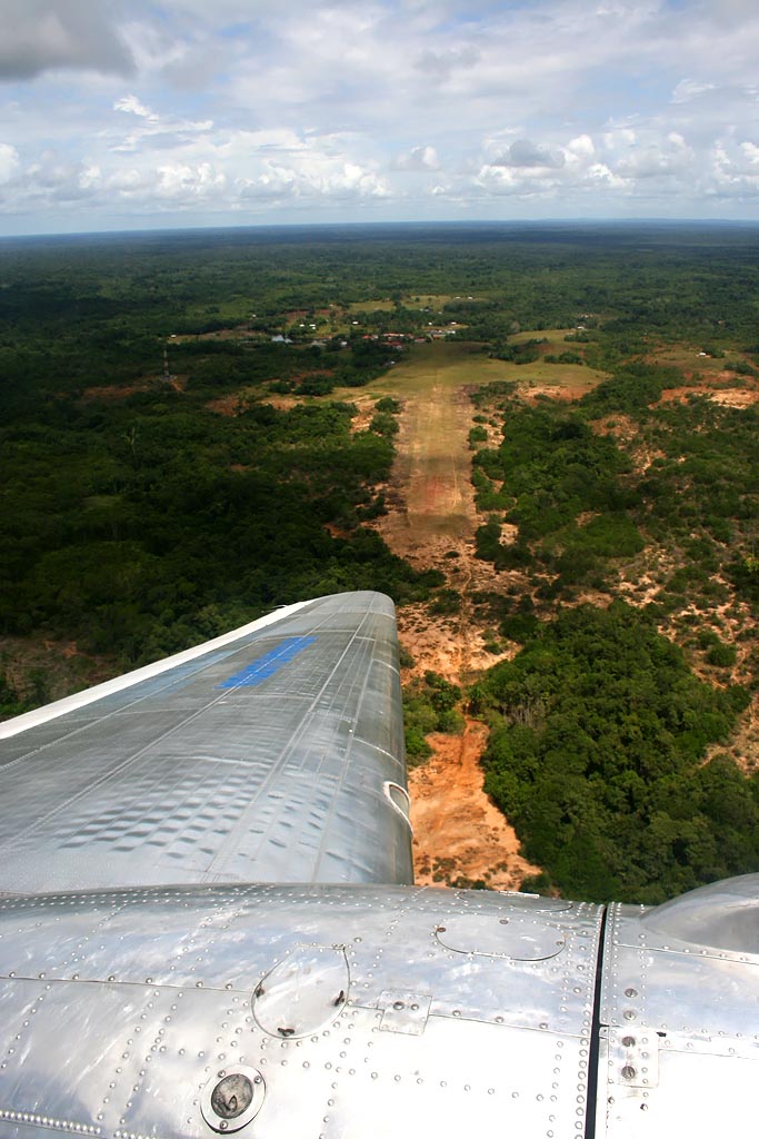 Virando sobre el campo de aterrizaje de Acaricuara. Si bien son muchas las pistas no preparadas que quedan en la selva colombiana, muchas de ellas han sido &quot;modernizadas&quot; por la Aerocivil, así que para ver una de éstas pistas hay que viajar un poco más al sur. El aterrizaje se hace en el sentido contrario a la perspectiva de ésta fotografía, así que un error puede terminar, o en el accidente de éste mismo avión en ésta pista, o contra la maleza al final del campo